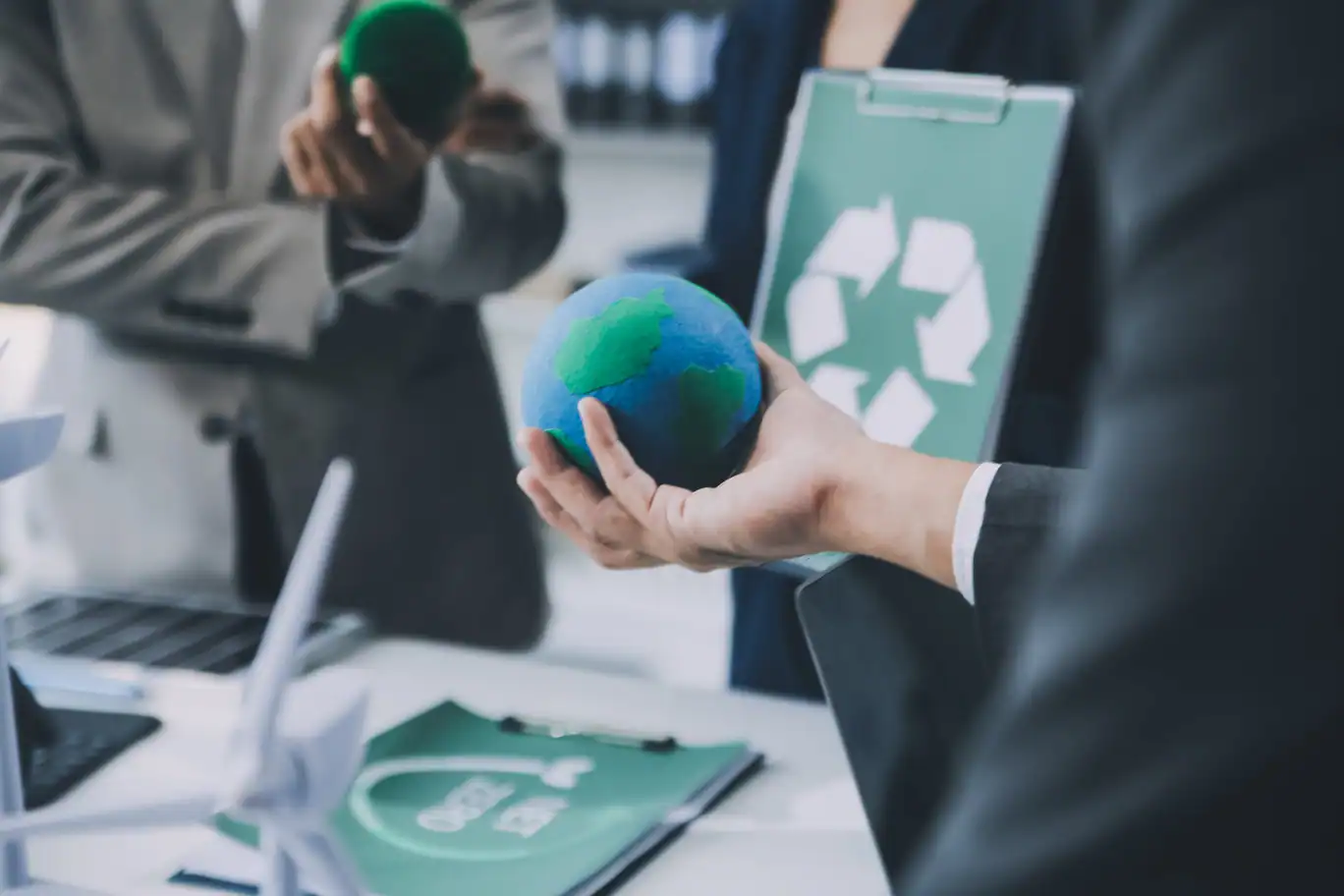 reunion-sostenibilidad-certificacion-iso-14001 Reunión sobre sostenibilidad con maqueta del planeta y símbolo de reciclaje, representando la diferencia entre cumplimiento legal e ISO 14001.